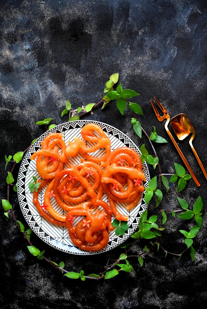 A beautifully arranged jalebi dessert garnished with greenery on a traditional plate.